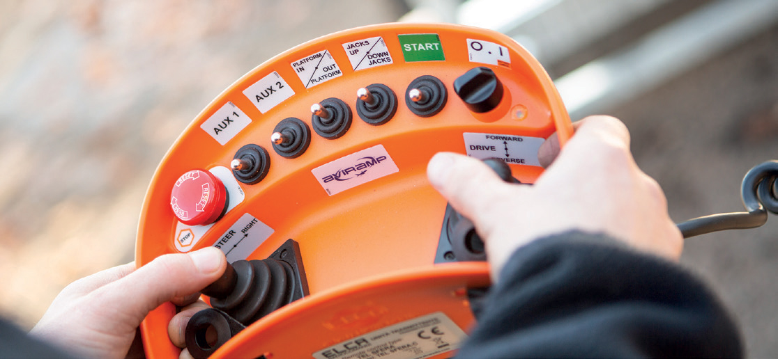 A professional holding a sophisticated remote control device, possibly used for operating a drone, remote-controlled vehicle, or industrial equipment. The remote has multiple buttons, switches, and joysticks, suggesting it is designed for precise and versatile control. The person’s hands are firmly gripping the device, indicating they are actively operating or preparing to operate the equipment. This setup is commonly seen in activities such as drone piloting, remote machinery operation, or remote-controlled hobbyist vehicles, emphasizing the importance of careful handling and coordination.