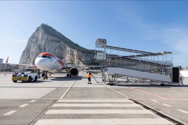 A picturesque tropical atmosphere, where passengers are about to embark on or have just arrived from a journey to a beautiful, warm destination. The airplane, set against the majestic mountain and bright blue sky, highlights the natural beauty of the region—perhaps an island paradise or coastal retreat. The presence of the aircraft suggests connectivity and adventure, inviting travellers to explore tropical beaches, lush landscapes, or vibrant local culture. The clear weather and scenic backdrop enhance the sense of relaxation and escape associated with tropical destinations. This image captures the seamless blend of modern aviation and stunning natural scenery, emphasizing the excitement and tranquillity of traveling to a tropical paradise.