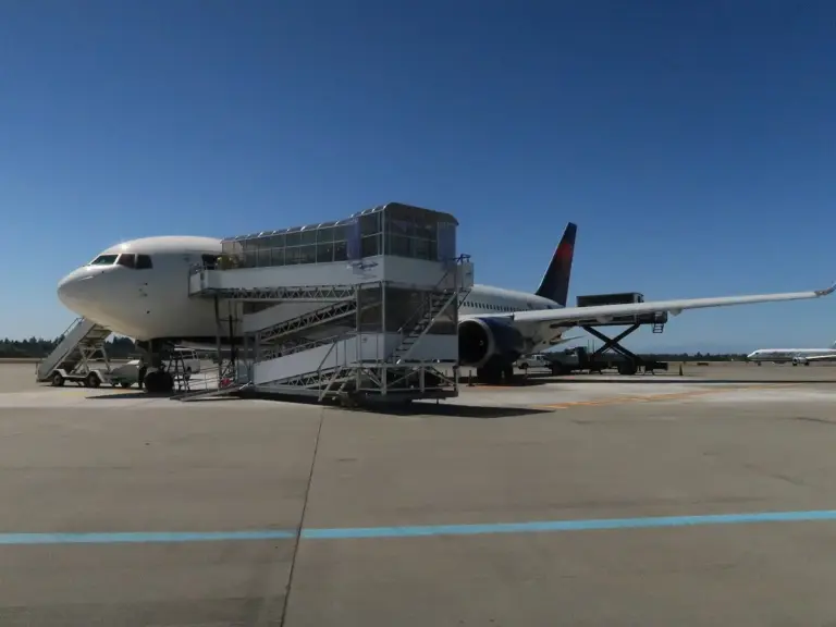 A moment of transition in air travel, where an airplane is parked on the tarmac, ready to welcome passengers. The boarding stairs positioned at the aircraft's door serve as a vital link between the ground crew and travelers, facilitating a smooth boarding process. The clear blue sky and the distant landscape—possibly mountains or open fields—add a sense of serenity and adventure, emphasizing the excitement of upcoming journeys. The bright sunlight and open space evoke feelings of optimism, exploration, and the thrill of discovering new destinations. This setup underscores the efficiency and organization behind commercial flights, showcasing the teamwork and planning that go into making air travel safe and comfortable. Whether it's a departure or arrival scene, it captures the anticipation and promise of travel, inviting viewers to imagine themselves embarking on an exciting trip to a distant place.