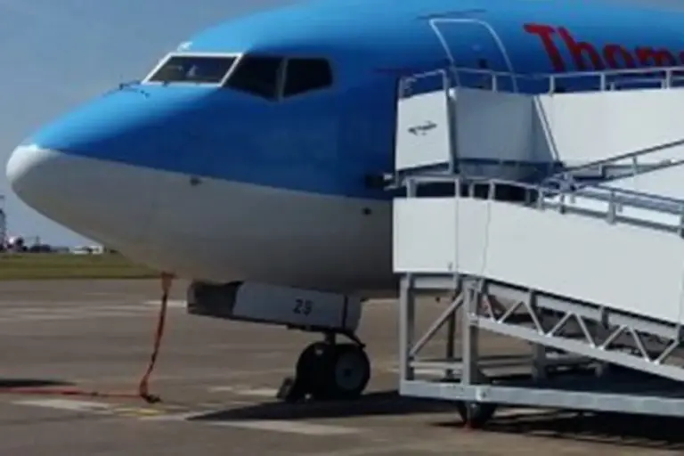 An airplane moving along the runway, likely during taxiing, with a mobile stairway attached to facilitate passenger boarding or disembarking. The scene suggests active airport operations, with the aircraft on the ground ready for or just after a flight. The background may include airport infrastructure or other aircraft, emphasizing the busy environment of air travel.