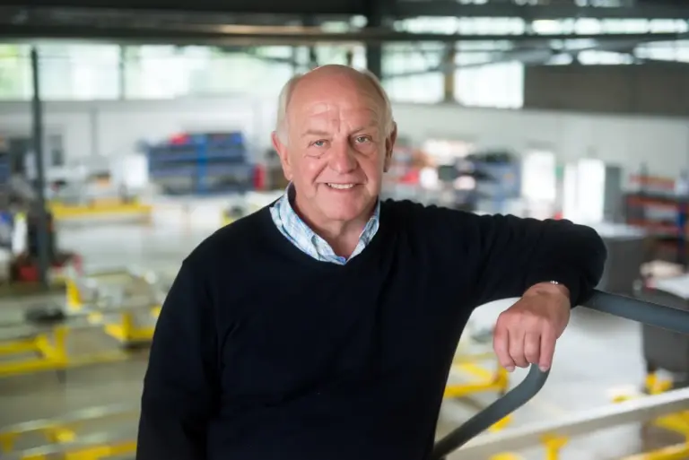 His confidence, experience, and approachability, embodying the spirit of a seasoned professional who’s comfortable in his environment. His relaxed smile and casual stance suggest he's at ease, perhaps enjoying the moment amidst a busy industrial setting.