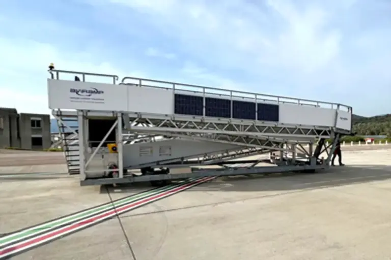 A crucial yet often overlooked part of the aviation experience—the mobile boarding staircase. Its sleek and functional design ensures safe and efficient passenger movement between the terminal and the aircraft, highlighting the behind-the-scenes efforts that make air travel seamless. Set against a backdrop of breath-taking mountains and expansive landscape, the scene evokes a sense of adventure and exploration. The partly cloudy sky and bright sunlight add a dynamic and inviting atmosphere, symbolizing optimism and the promise of new journeys. The presence of the staircase on the tarmac signifies readiness and operational efficiency, reflecting the meticulous planning and coordination involved in airline operations. It also emphasizes the harmony between technology and nature, reminding us that while air travel is highly advanced, it is still closely connected to the natural world. Overall, this image inspires feelings of wanderlust and adventure, capturing a moment of anticipation just before take-off, where travellers are about to embark on an exciting journey to distant places.