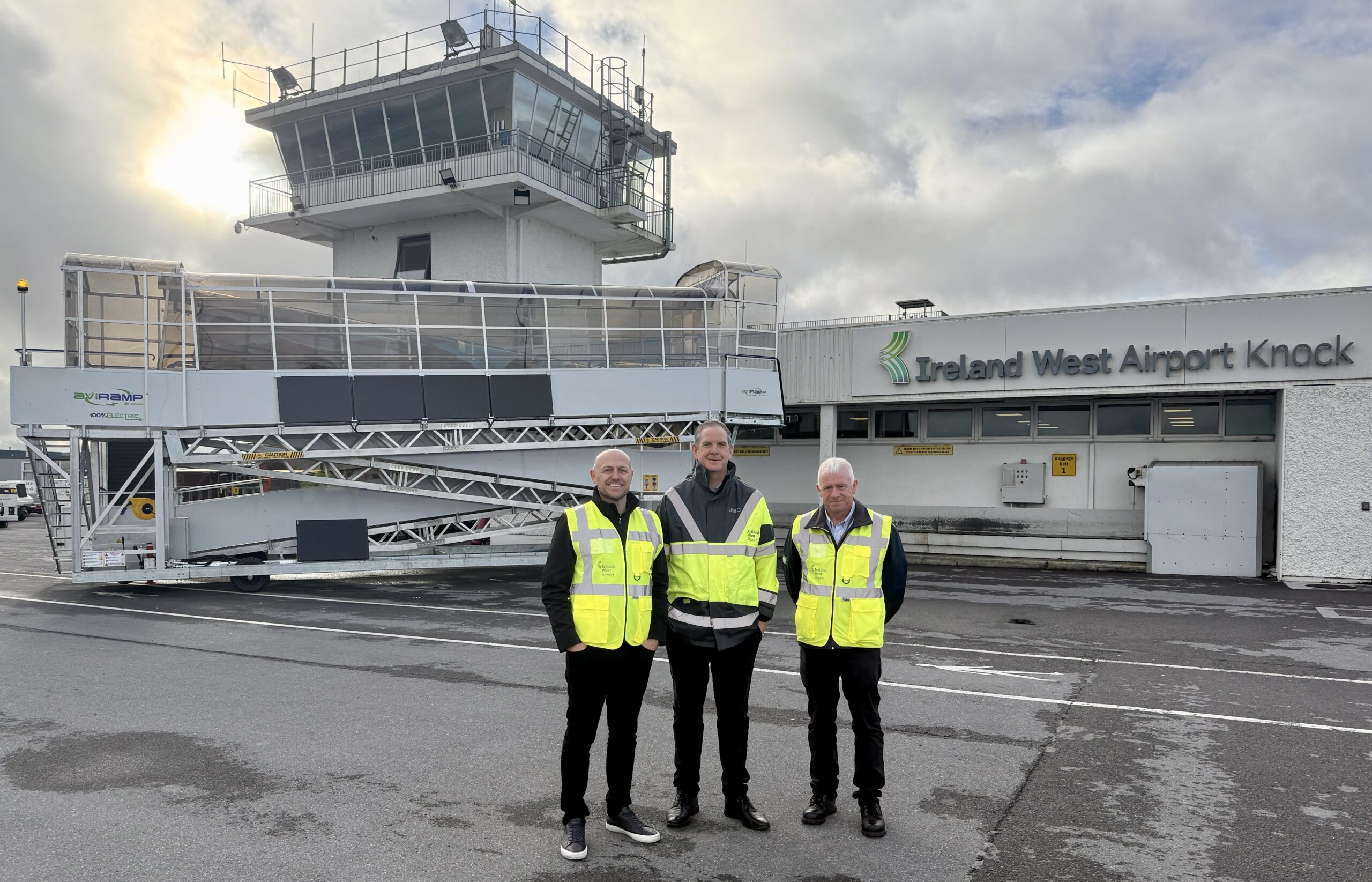 Three men in high visibility jackets standing in front of an aircraft boarding ramp at Ireland West Airport