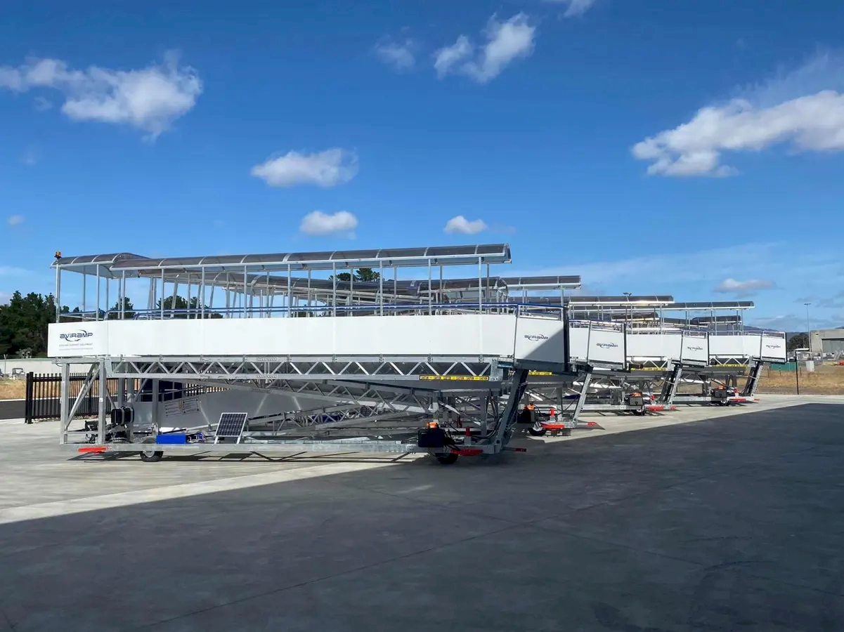 Several mobile passenger stairs positioned on the airport tarmac, prepared for boarding or disembarking aircraft, set against a bright blue sky with scattered clouds.