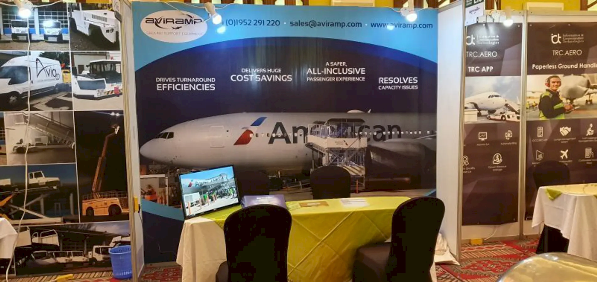 A trade show booth displaying aviation services and ground handling solutions, with large banners featuring images of aircraft and equipment, as well as a table and chairs for discussions.