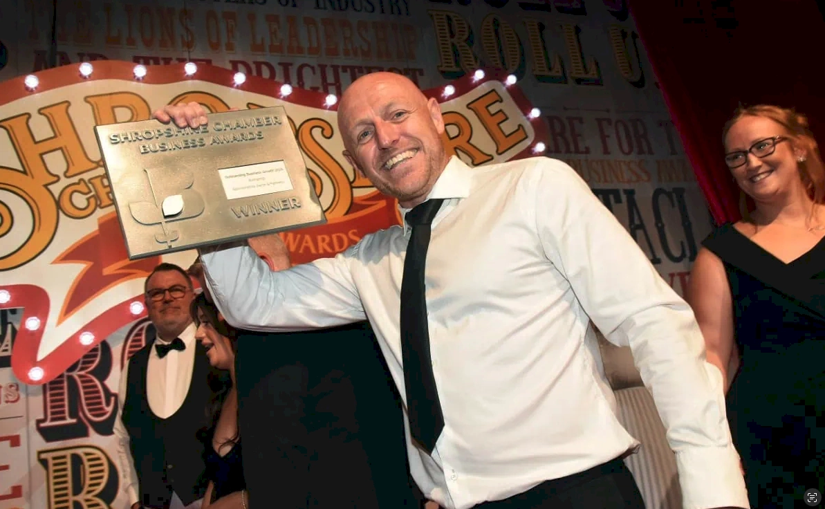 Celebrating success: a man proudly displays a giant check trophy during an awards event, surrounded by enthusiastic teammates.