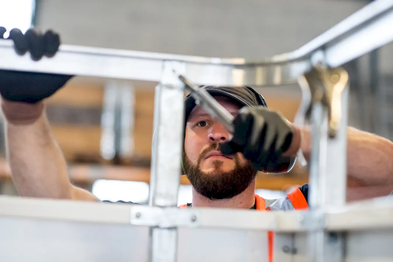 The dedication and physical prowess of a burly worker engaged in hands-on labour. His muscular build and focused expression reflect a commitment to craftsmanship and the importance of skilled manual work in industrial, construction, or manufacturing settings. Clad in workwear suited for heavy-duty tasks, he demonstrates strength and resilience, essential qualities for handling demanding jobs that require precision and physical effort. The tools in his hands, such as a wrench, signify technical expertise and the importance of attention to detail in maintenance or assembly work. The background may include industrial machinery, tools, or workshop elements, emphasizing a bustling environment where productivity and safety are paramount. This image celebrates hardworking individuals who keep industries running smoothly, embodying strength, skill, and dedication that form the backbone of many essential services and infrastructure.