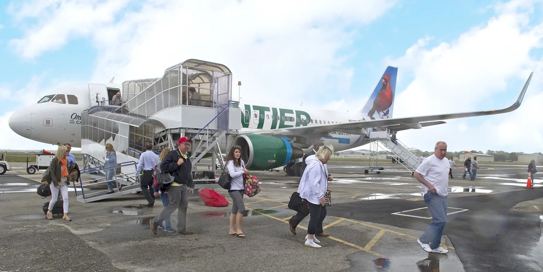 Passengers leaving the Frontier Airlines plane using a mobile staircase after arriving at the airport, with rain falling.