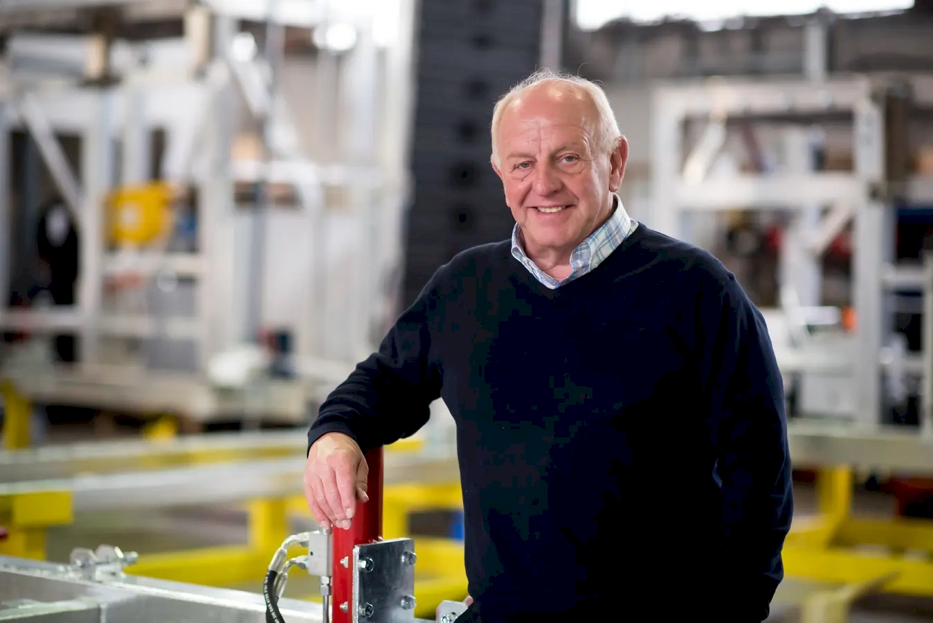 His confidence, experience, and approachability, embodying the spirit of a seasoned professional who’s comfortable in his environment. His relaxed smile and casual stance suggest he's at ease, perhaps enjoying the moment amidst a busy industrial setting. His attire—a simple, smart-casual sweater over a collared shirt—reflects a balance of professionalism and laid-back attitude, indicating he's someone who takes his work seriously but also knows how to stay relaxed and approachable. The background hints at a technical or manufacturing environment, possibly where he’s been honing his skills over years, making him a valuable source of knowledge and mentorship. Overall, he radiates a sense of calm confidence, showing that experience and expertise don’t have to come with stiffness—sometimes, being "chilled" is the perfect mindset for tackling complex projects with a steady hand and positive outlook. He’s the kind of person who inspires trust and camaraderie in a work environment, blending competence with a relaxed, friendly vibe.