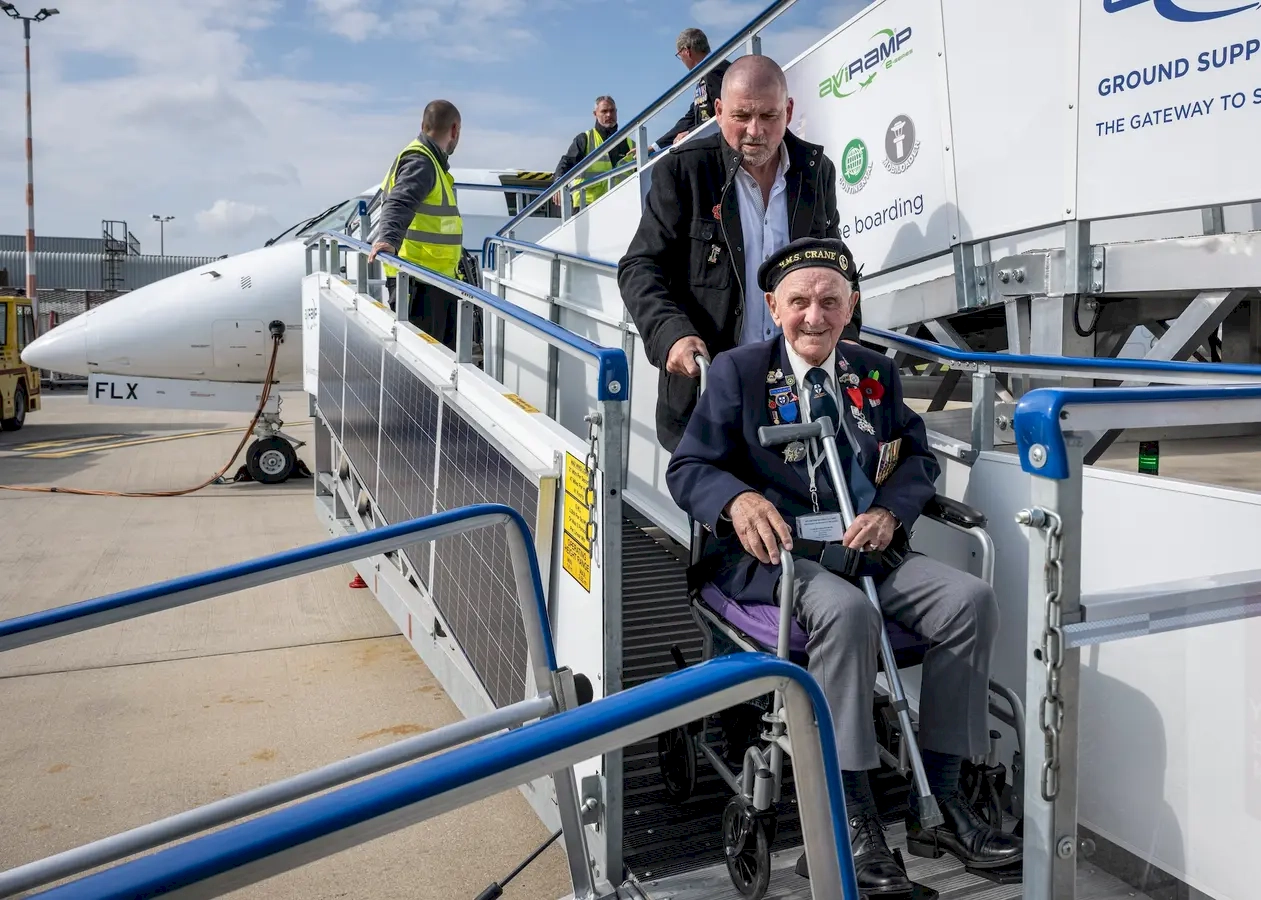 A heartfelt moment that highlights appreciation and respect for veterans. The elderly veteran, dressed in a uniform, symbolizes service, sacrifice, and dedication to the country. His warm smile and waving gesture reflect gratitude, pride, and perhaps a sense of accomplishment or nostalgia. Airport staff assisting him demonstrate the respect and care extended to veterans, ensuring that their travel experience is comfortable and dignified. The supportive environment emphasizes the importance of honoring those who have served, recognizing their contributions. The background, with people and airport activities, adds to the lively and respectful atmosphere of the scene. Overall, this moment captures the emotional connection between service and gratitude, celebrating veterans in a setting that signifies new beginnings, reunions, or journeys—underscoring the nation's appreciation for their sacrifices.