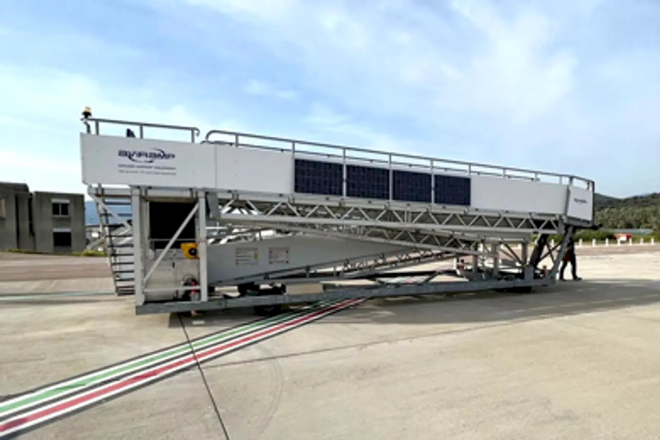 A crucial yet often overlooked part of the aviation experience—the mobile boarding staircase. Its sleek and functional design ensures safe and efficient passenger movement between the terminal and the aircraft, highlighting the behind-the-scenes efforts that make air travel seamless. Set against a backdrop of breath-taking mountains and expansive landscape, the scene evokes a sense of adventure and exploration. The partly cloudy sky and bright sunlight add a dynamic and inviting atmosphere, symbolizing optimism and the promise of new journeys. The presence of the staircase on the tarmac signifies readiness and operational efficiency, reflecting the meticulous planning and coordination involved in airline operations. It also emphasizes the harmony between technology and nature, reminding us that while air travel is highly advanced, it is still closely connected to the natural world. Overall, this image inspires feelings of wanderlust and adventure, capturing a moment of anticipation just before take-off, where travellers are about to embark on an exciting journey to distant places.